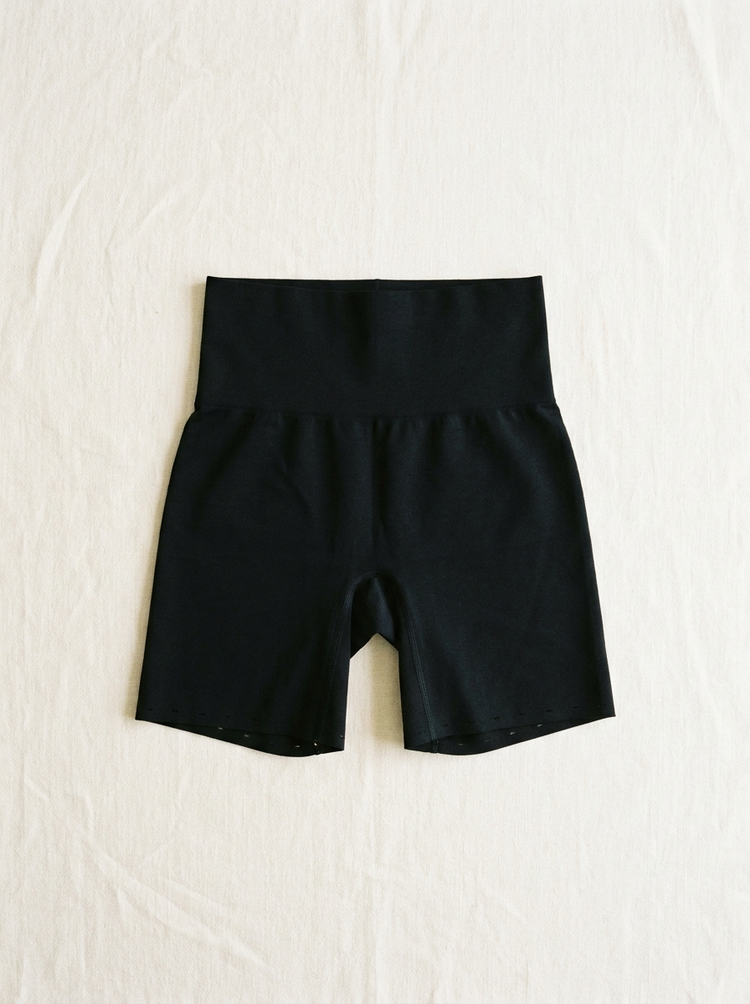 Short moldeador negro extendido en plano sobre lino, con el talle alto y el bajo a láser visibles